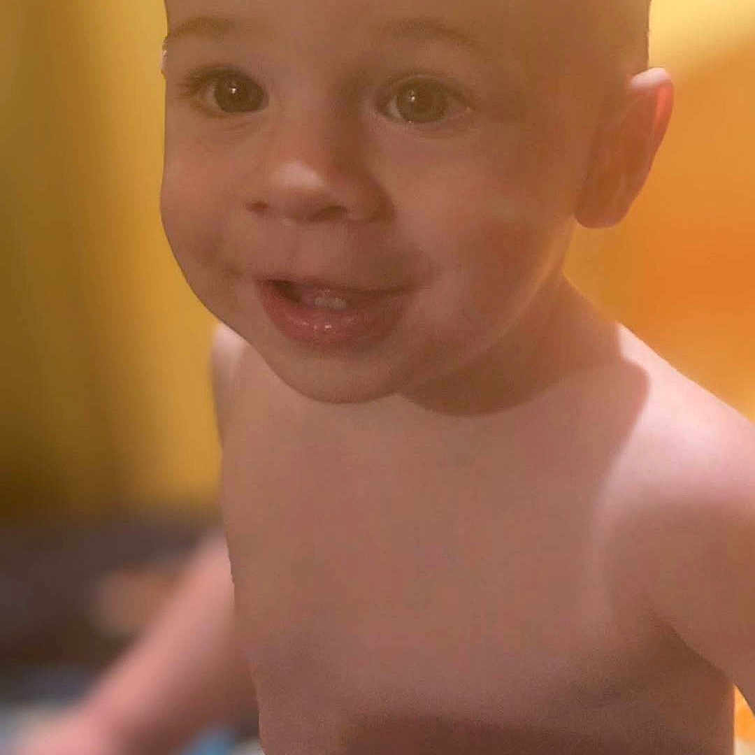 Hudson is registered to the contest to win money with this photo: toddler, child, smile, face, bare_chest, young_child, portrait, indoors, warm_lighting, yellow_background, happy, cute, baby, skin, head, eyes, young, expression, person, human