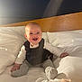 baby, smiling, bed, pillow, white_bedding, wooden_headboard, infant, happy, child, indoor, cute, sitting, portrait, cozy, soft_light, clothing, sock, person, cheerful, young_child