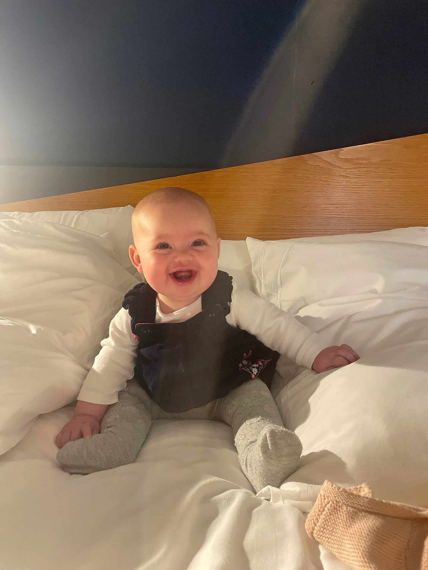 Alys joined the competition — help win amazing prizes! baby, smiling, bed, pillow, white_bedding, wooden_headboard, infant, happy, child, indoor, cute, sitting, portrait, cozy, soft_light, clothing, sock, person, cheerful, young_child