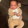 baby, infant, child, couch, clothing, nike, jacket, pants, socks, fist, face, curly_hair, indoor, plush_furniture, relaxed, portrait, cute, young_child, comfort, seated
