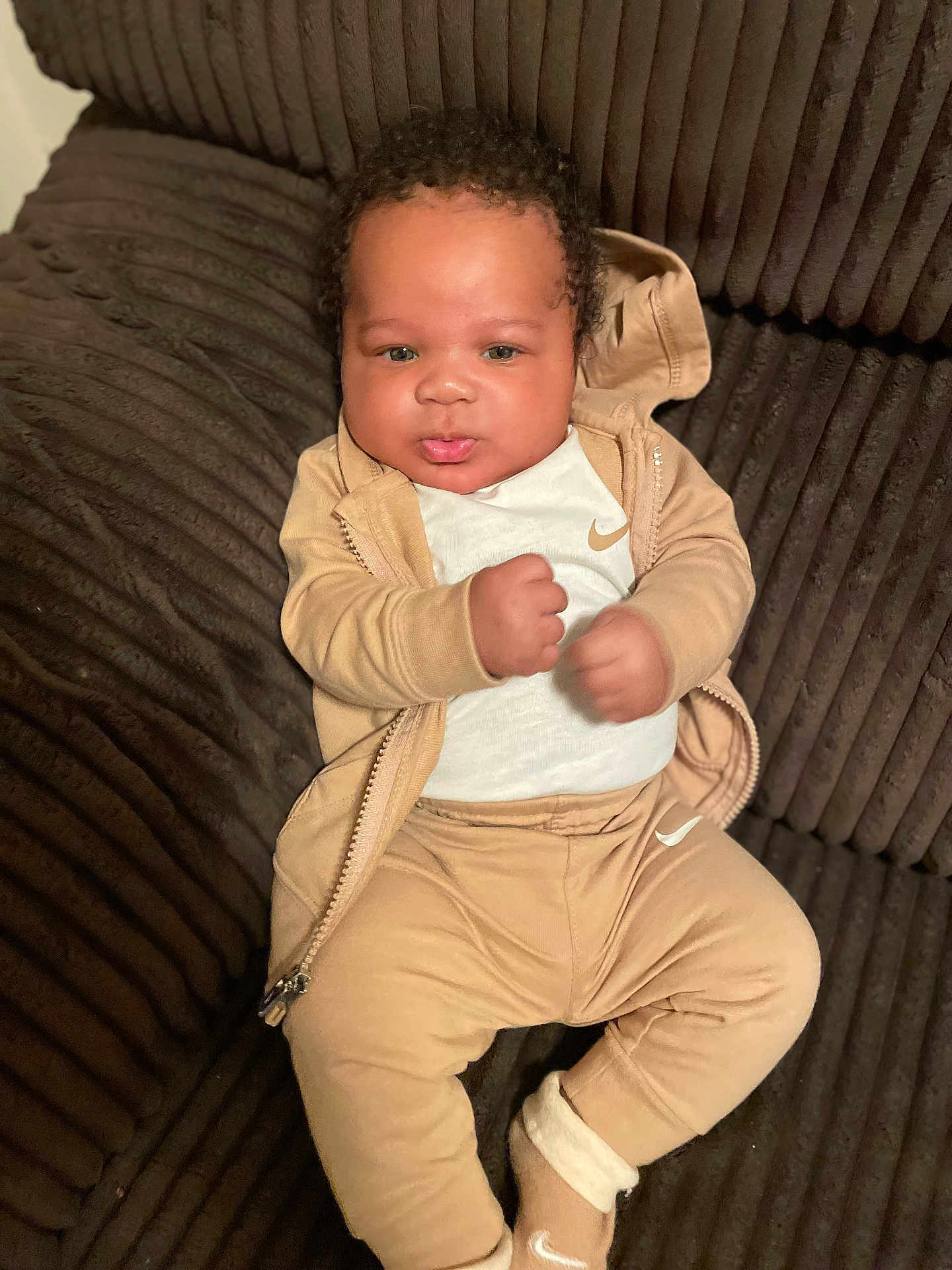 Kaiden Aka Kg is registered to the contest to win money with this photo: baby, infant, child, couch, clothing, nike, jacket, pants, socks, fist, face, curly_hair, indoor, plush_furniture, relaxed, portrait, cute, young_child, comfort, seated