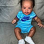 baby, child, sitting, nike, blue_outfit, white_sneakers, curly_hair, couch, indoor, portrait, smiling, cute, infant, clothing, footwear, person, young_child, fashion, happy, casual