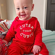 Parker joined the competition — help win amazing prizes! baby, child, red_clothing, onesie, smile, happy, indoors, bed, blanket, foot, hand, face, cute, sitting, infant, person, skin, room, door, text_print