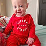 baby, child, red_clothing, onesie, smile, happy, indoors, bed, blanket, foot, hand, face, cute, sitting, infant, person, skin, room, door, text_print