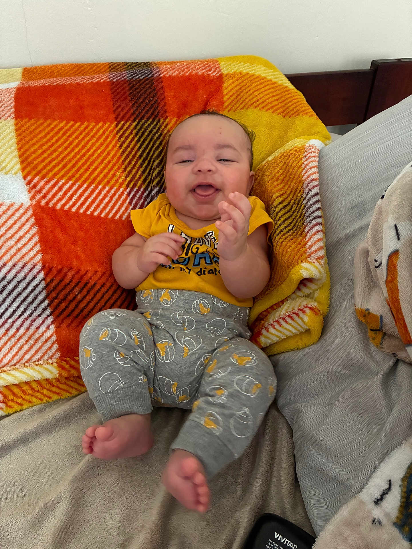 Papalovy joined the competition — help win amazing prizes! baby, infant, clothing, yellow_shirt, gray_pants, blanket, plaid, orange, yellow, bed, cushion, smiling, happy, person, feet, hands, head, indoors, furniture, cute