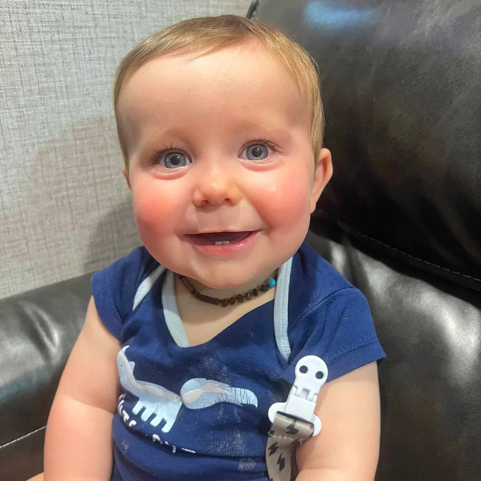 Waylan joined the competition — help win amazing prizes! baby, child, smile, blue_eyes, rosy_cheeks, navy_shirt, pacifier_clip, skull_design, leather_couch, indoor, close_up, happy, cute, infant, person, portrait, seated, short_hair, necklace, bright_eyes
