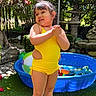 barefoot, beach_ball, child, clapping, daylight, flowers, garden, girl, grass, happy, kiddie_pool, nature, outdoor, plants, playing, smiling, summer, sunlight, water_toy, yellow_swimsuit