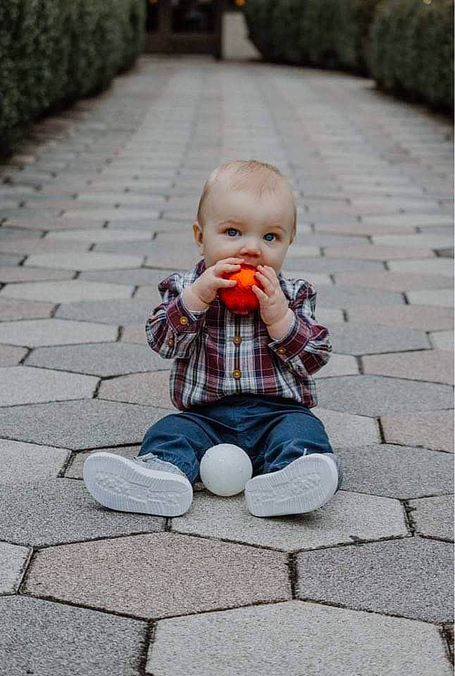 Kayce is registered to the contest to win money with this photo: asphalt, baby, child, cobblestone, doll, flooring, grass, leisure, person, plant, public_space, road_surface, sidewalk, sitting, spring, standing, toddler, toy, vertebrate, wall