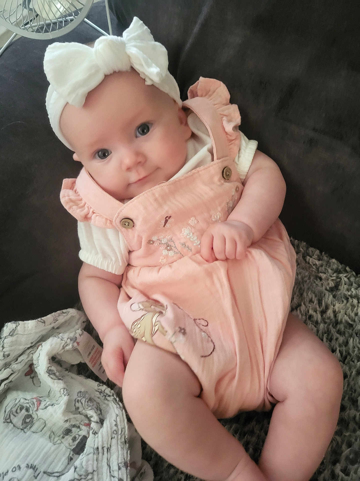 Lyra-Lily is registered to the contest to win money with this photo: baby, infant, headband, bow, romper, pink_clothing, couch, blanket, cartoon_print, smiling, chubby_cheeks, child, indoor, portrait, seated, curious, cute, soft_lighting, closeup, person