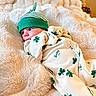 Holden is registered to the contest to win money with this photo: baby, infant, blanket, green_hat, onesie, clothing, shamrock, pattern, plush_toy, frog, soft_texture, bedroom, cozy, cute, portrait, child, laying_down, warm, comfortable, curious