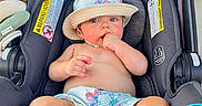 Holden is registered to the contest to win money with this photo: baby, child, car_seat, hat, bare_chest, shorts, foot, hand, face, skin, indoors, seat, clothing, person, infant, cute, sitting, summer, relaxing, sunhat