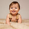 baby, smiling, happy, infant, overalls, cute, portrait, fur_rug, soft_lighting, cheerful, child, crawling, indoors, skin, face, young_child, expression, adorable, person, warm_colors