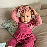 toddler, child, pink_bow, pink_outfit, sitting, couch, indoor, portrait, cute, baby, hands_on_head, serious_expression, cozy, headband, long_sleeves, cushion, soft_lighting, casual, home, fashion