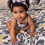baby, child, curly_hair, headband, leopard_print, bedspread, crawling, indoor, cute, playful, person, infant, fashion, pattern, smiling, skin, hand, footwear, bed, pillow
