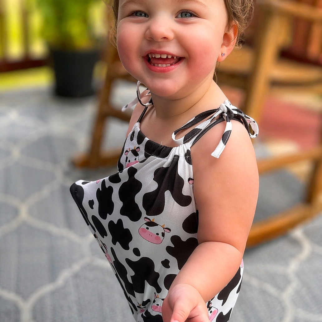 Amelia is registered to the contest to win money with this photo: toddler, child, smiling, pigtails, cow_print, clothing, barefoot, indoor, carpet, furniture, plant, portrait, cute, happy, young_child, person, fashion, playful, baby, room