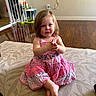 baby_gate, carpet, child, clapping_hands, cross_legged, curly_hair, cute, floor, girl, home, indoor, pink_dress, portrait, power_outlet, sitting, smiling, toddler, toys, wall, wooden_floor