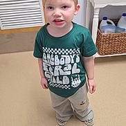 Graylen is registered to the contest to win money with this photo: child, toddler, green_shirt, standing, indoor, floor, door, plant, basket, sign, expression, clothing, sneakers, checkered, hair, person, young_child, casual_wear, home_interior, furniture