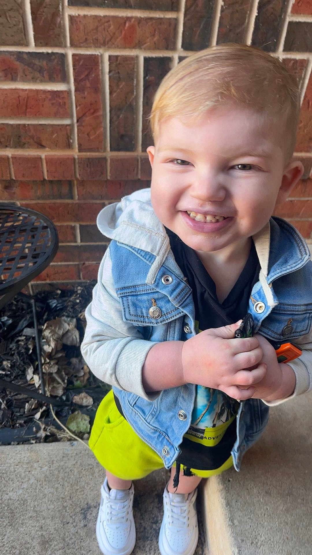 Graylen joined the competition — help win amazing prizes! child, toddler, smiling, blonde_hair, denim_jacket, yellow_shorts, white_shoes, outdoor, brick_wall, concrete, happy, person, standing, holding, casual_clothing, daylight, metal_chair, expression, cute, portrait