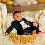 Ivaan joined the competition — help win amazing prizes! baby, tuxedo, basket, gift_box, white_rug, flooring, indoors, child, portrait, clothing, person, cute, formal_wear, infant, furniture, smile, celebration, holiday, decor, relaxing