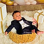 baby, tuxedo, basket, gift_box, white_rug, flooring, indoors, child, portrait, clothing, person, cute, formal_wear, infant, furniture, smile, celebration, holiday, decor, relaxing