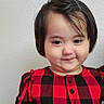 child, toddler, smile, red_dress, black_and_red, plaid, portrait, indoors, short_hair, buttoned_dress, cute, funny_expression, person, wall, standing, young_child, female, light_skin, fashion, casual