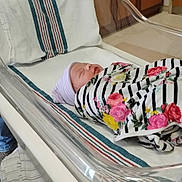 Destinee is registered to the contest to win money with this photo: newborn, baby, hospital, bassinet, blanket, striped, floral, sleeping, towel, hat, person, adult, hospital_room, cabinet, floor, medical_equipment, comfort, indoor, rest, care