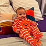 Angel joined the competition — help win amazing prizes! baby, infant, smiling, orange_clothing, striped_onesie, pumpkin_design, couch, pillows, home_interior, cute, child, happy, sitting, cozy, soft_fabric, texture, plush, indoor, portrait, face