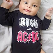 Isaac participe au concours pour gagner de l'argent avec cette photo : arms, baby, bed, bedding, black_clothing, child, cute, face, happy, indoor, infant, legs, lying_down, onesie, person, skin, smile, soft_light, text_on_clothing, young