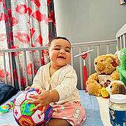 Wahenoor is registered to the contest to win money with this photo: baby, ball, bed, cactus_toy, cardigan, child, colorful, curtain, floral_pattern, happy, indoor, nursery, person, photography, play, skirt, smiling, stuffed_animal, teddy_bear, toy