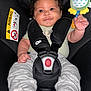 baby, car_seat, child, toy, smile, curly_hair, safety_harness, infant, cute, holding, clothing, pacifier, happy, indoor, seat_belt, colorful_toy, person, close_up, portrait, baby_toy