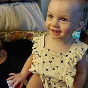 Serenity is registered to the contest to win money with this photo: toddler, child, smile, sitting, couch, clothing, heart_pattern, person, hand, face, indoors, wall, cushion, happy, baby, cute, portrait, blurred, light, skin