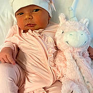 Paisley is registered to the contest to win money with this photo: baby, newborn, infant, child, portrait, face, serious_expression, pink_outfit, knit_hat, bow, plush_toy, llama, stuffed_animal, blanket, indoor, sitting, close_up, soft_lighting, pastel_colors, nursery