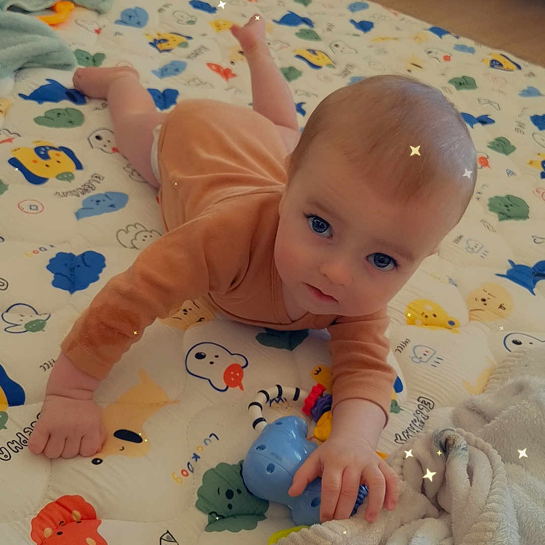 ézio a rejoint le concours — aidez-le/la à gagner de superbes lots ! baby, infant, playmat, toy, blanket, floor, indoor, child, cute, reaching, animal_prints, blue_toy, soft_lighting, cozy, curious, lying_down, home, person, small_hands, sparkles