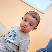 Legend is registered to the contest to win money with this photo: toddler, child, indoor, pajamas, grey_clothing, curious_expression, face, person, window, adult_arm, blue_sleeve, peach_wall, sign, no_smoking, casual, leaning, young_child, short_hair, light, seated