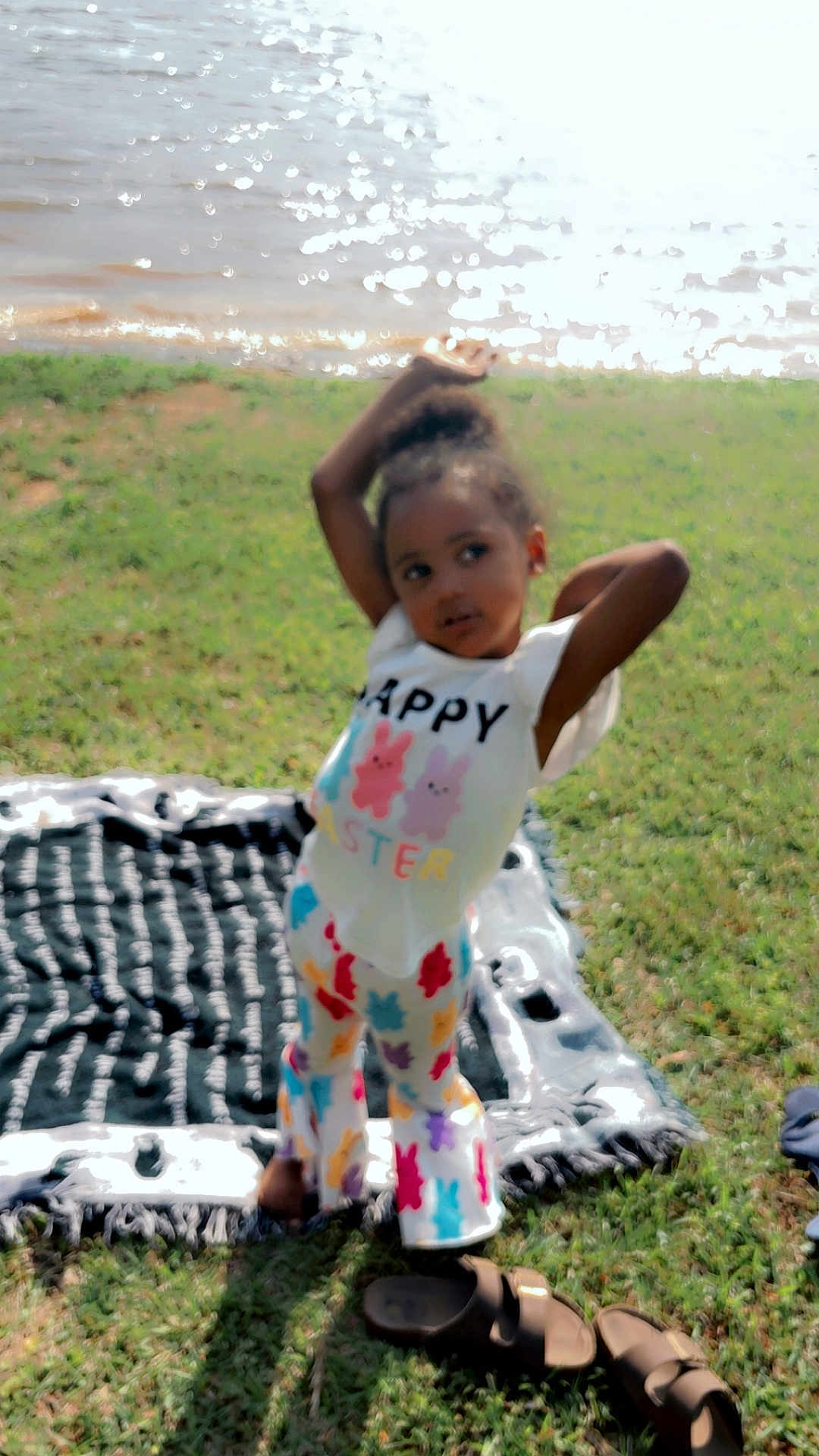 Adalynn is registered to the contest to win money with this photo: child, grass, water, blanket, sandals, outdoor, toddler, clothing, colorful, pose, playful, sunlight, nature, happy_easter, patterned_pants, smiling, daylight, relaxation, casual, summer
