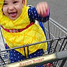 baby, barefoot, blue_clothing, building, child, costume, fun, hand_raised, happy, metal_cart, outdoor, parking_lot, pineapple, polka_dots, shopping_cart, sidewalk, smiling, tongue_out, urban, yellow