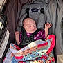 newborn, baby, sleeping, stroller, blanket, crocheted_blanket, purple_clothing, infant, child, car_seat, safety_harness, peaceful, resting, indoors, soft_light, cute, small_hands, head, face, cozy