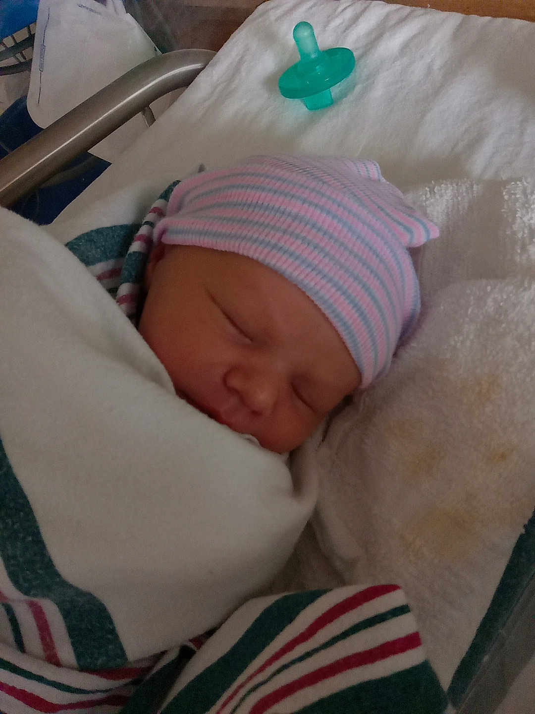 Mckinley is registered to the contest to win money with this photo: newborn, baby, sleeping, blanket, hospital, pacifier, hat, striped_hat, infant, swaddled, towel, face, child, bed, resting, cute, person, peaceful, closeup, indoors
