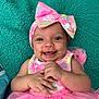 baby, smiling, pink_dress, headband, bow, happy, infant, cute, child, portrait, hands, lying_down, teal_blanket, tulle_skirt, colorful_clothing, indoors, skin, face, eyes, person