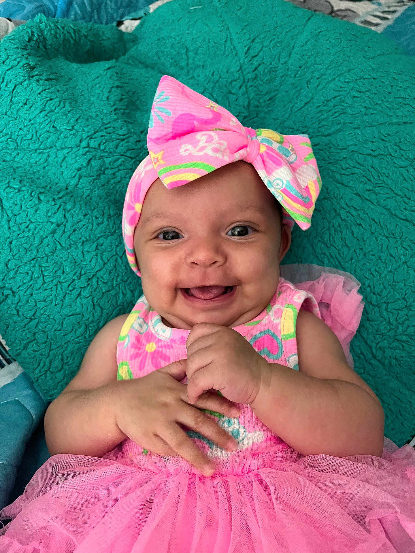 Shyonna joined the competition — help win amazing prizes! baby, smiling, pink_dress, headband, bow, happy, infant, cute, child, portrait, hands, lying_down, teal_blanket, tulle_skirt, colorful_clothing, indoors, skin, face, eyes, person