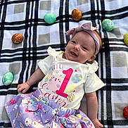 Everleigh joined the competition — help win amazing prizes! baby, child, smiling, plaid_blanket, easter_eggs, headband, purple_skirt, shirt, outdoor, holiday, celebration, cute, infant, lying_down, festive, spring, colorful, happy, person, portrait