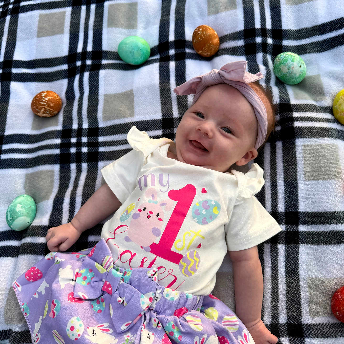 Everleigh joined the competition — help win amazing prizes! baby, child, smiling, plaid_blanket, easter_eggs, headband, purple_skirt, shirt, outdoor, holiday, celebration, cute, infant, lying_down, festive, spring, colorful, happy, person, portrait