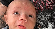 Azrael is registered to the contest to win money with this photo: baby, infant, onesie, shark_pattern, person, tattoo, tshirt, graphic_tshirt, face, skin, eyes, mouth, expression, hand, clothing, indoor, portrait, closeup, child, newborn