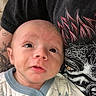 baby, infant, onesie, shark_pattern, person, tattoo, tshirt, graphic_tshirt, face, skin, eyes, mouth, expression, hand, clothing, indoor, portrait, closeup, child, newborn