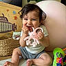 baby, basket, chewing, child, colorful, couch, curly_hair, cute, decor, green, happy, indoor, infant, person, pink, playtime, smiling, soft_surface, teether, toy