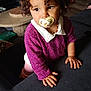 toddler, child, pacifier, curly_hair, purple_sweater, indoor, couch, television, thoughtful, brown_eyes, necklace, hand, furniture, floor, home, portrait, clothing, baby, cozy, casual