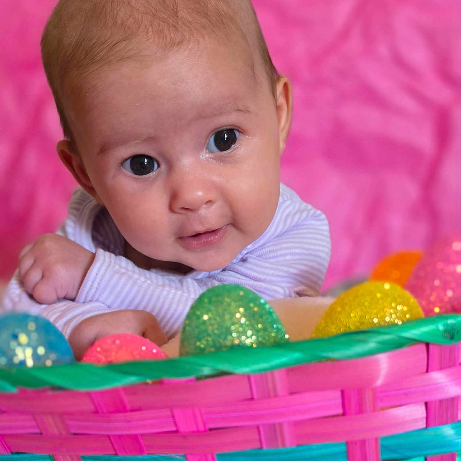 Skylar joined the competition — help win amazing prizes! baby, infant, easter_basket, colorful, sparkling_eggs, pink_background, cute, portrait, child, smiling, curious, closeup, face, hands, woven_basket, holiday, festive, bright, happy, indoors