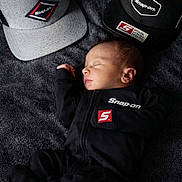 River Dudley is registered to the contest to win money with this photo: baby, babywear, black_clothing, blanket, branding, cap, closeup, cute, hat, headwear, indoor, infant, logo, newborn, peaceful, portrait, resting, sleeping, snapon, soft_texture