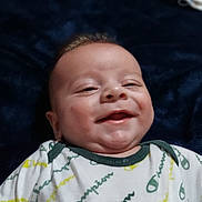 River Dudley is registered to the contest to win money with this photo: baby, smiling, infant, onesie, clothing, champion, blanket, portrait, happy, face, child, cute, lying_down, baby_garment, young_child, indoors, soft_lighting, skin, expression, cozy