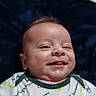 River Dudley joined the competition — help win amazing prizes! baby, infant, smile, tongue, onesie, clothing, champion, face, head, lying_down, blanket, fabric, pattern, cheerful, skin, cute, child, portrait, indoor, soft